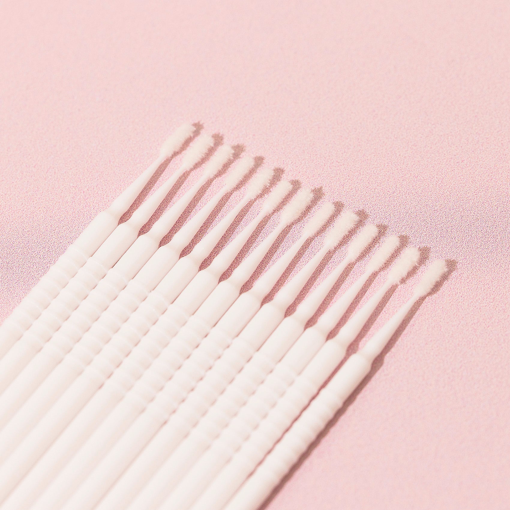 13 white Disposable Micro Applicators over a pink background.