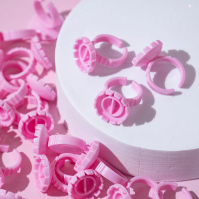 Pink Glue Rings scattered on a pink surface with some displayed on a white circular platform.