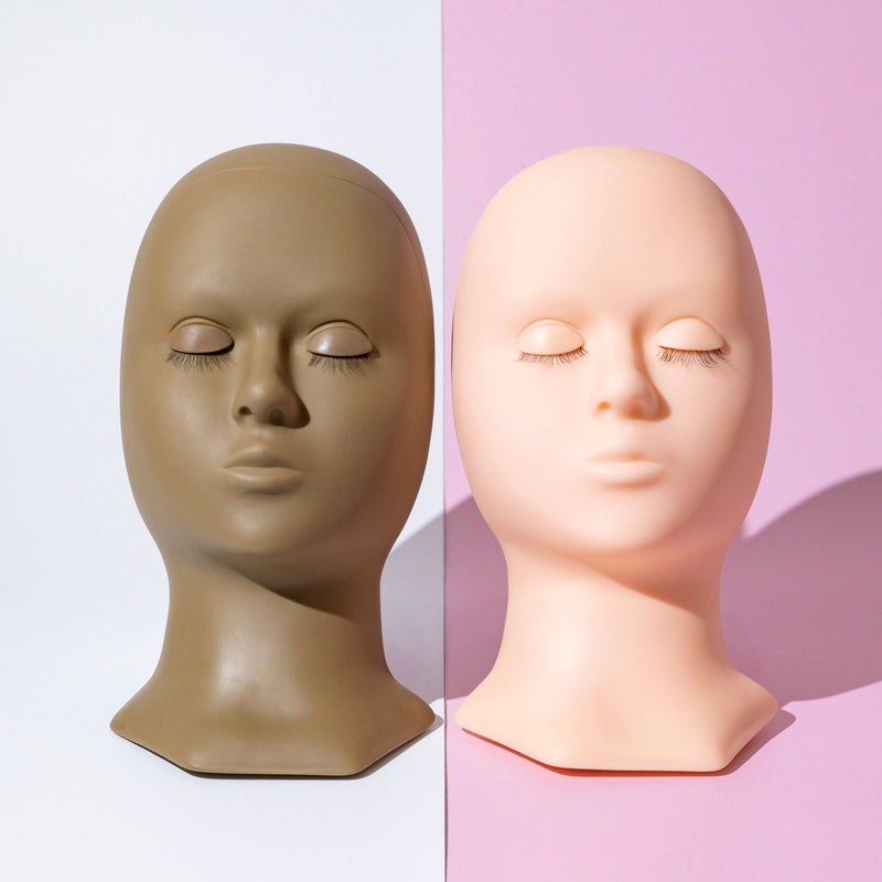 Two lash training mannequin heads in dark and light, side by side with closed eyes, ideal for practicing eyelash extensions.