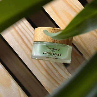 Green eyebrow mask displayed on a wooden background with a leaf