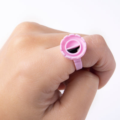 A pink glue ring with a divider filled with glue, worn on a hand against a white background.