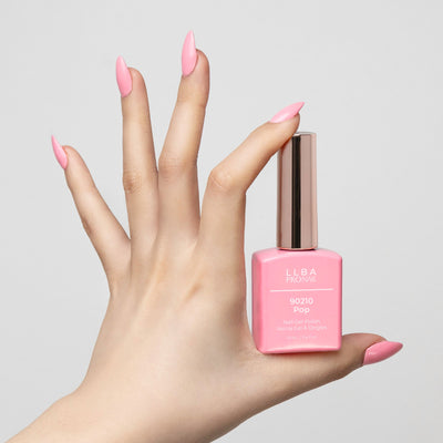 Hand with long, pink nails holding LLBA ProNail 90210 Pop nail gel polish in a matching pink shade, against a white background.