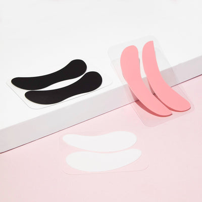 Curacoro lash pads in black, pink, and white variations, displayed on a white platform with a pink background.