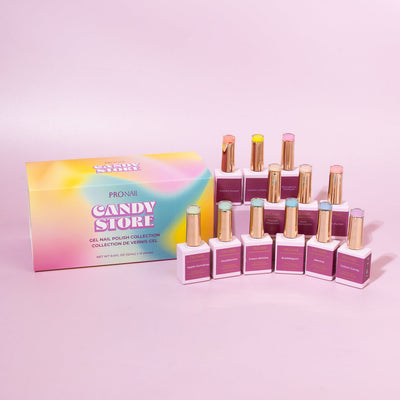 A collection of nail polish bottles with gold caps arranged beside a colorful "Candy Store" box on a pastel pink background.