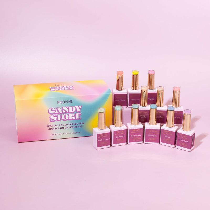 A collection of nail polish bottles with gold caps arranged beside a colorful "Candy Store" box on a pastel pink background.