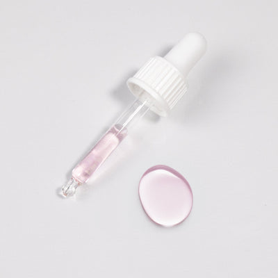 Curacoro Adhesive Speed Booster dropper with pink liquid and a droplet on a white surface.