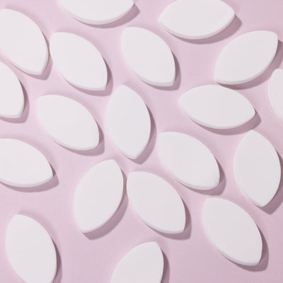 Stack of White Lash Practice Sponge pieces over a light pink background. 