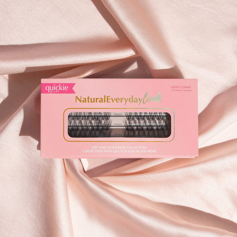 Pink lash extension kit box with transparent window showing three rows of lash clusters in different lengths, placed on soft, peach-colored fabric.