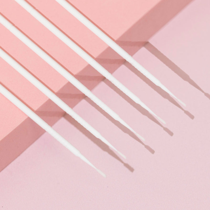 Close-up of white disposable micro applicators placed diagonally on a light pink and beige surface.