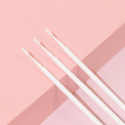 Close-up of white disposable micro applicators placed diagonally on a light pink and beige surface.