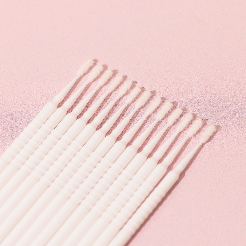 13 white Disposable Micro Applicators over a pink background. 