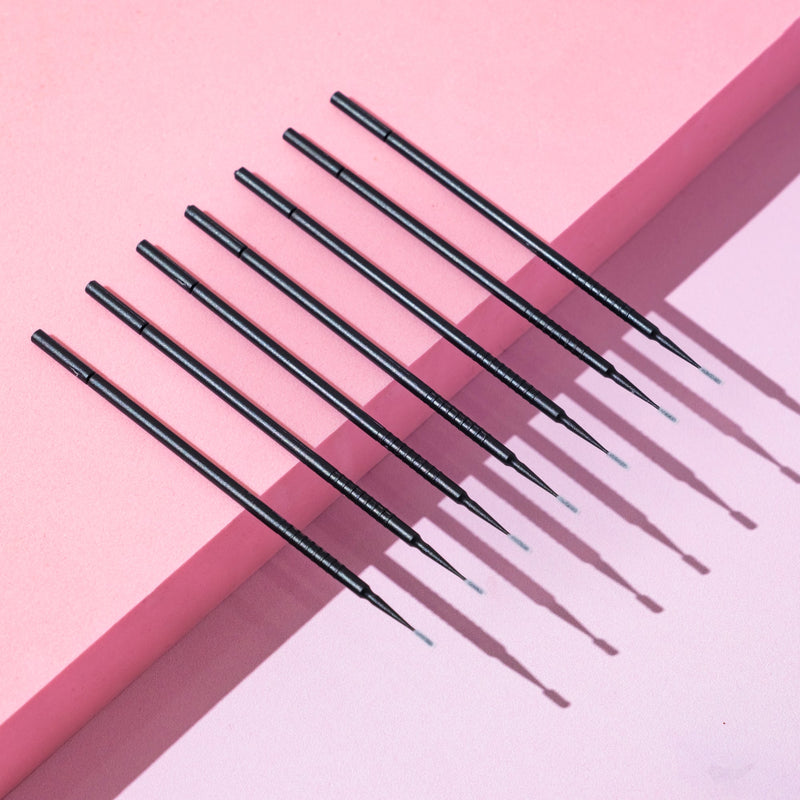 Black disposable micro applicators placed diagonally on a light pink and beige surface.