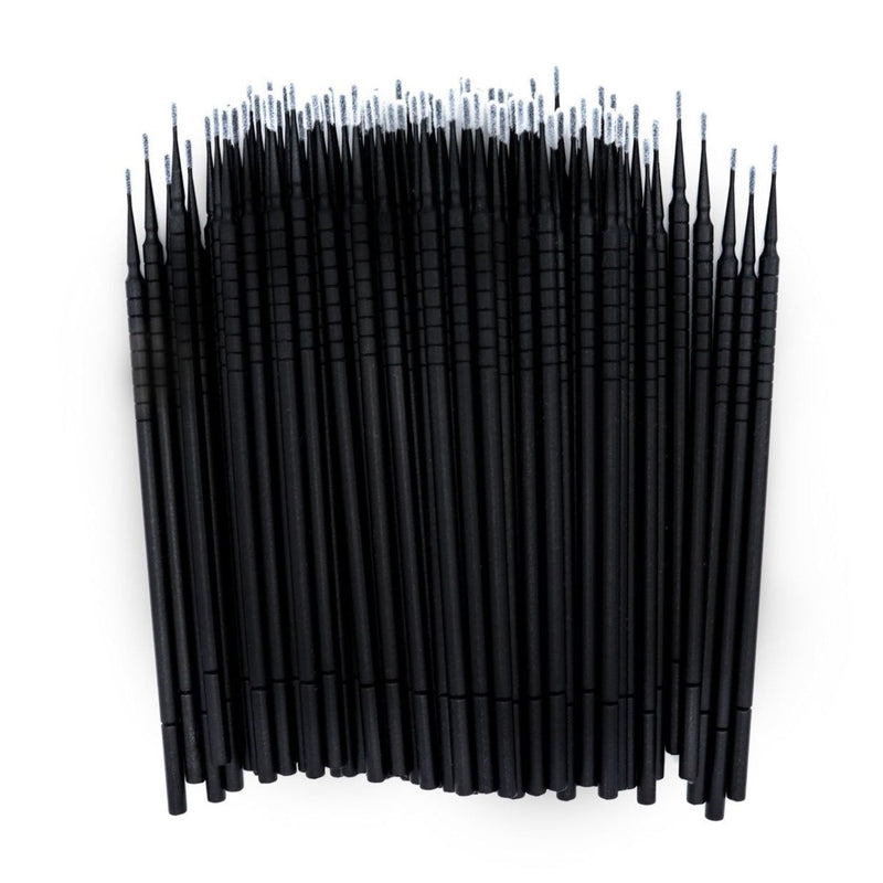 Close-up of black disposable micro applicators with fine white tips arranged vertically on a white background.