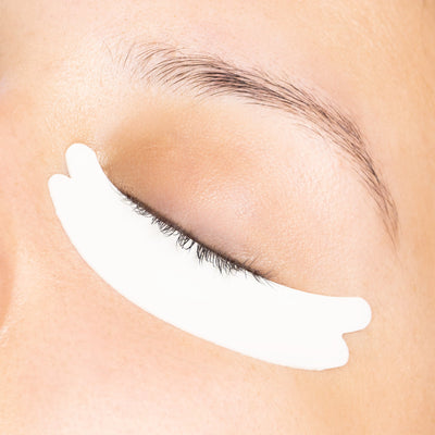 A close-up of a model's closed eye with a hypoallergenic foam under-eye pad applied to the lower eyelid, emphasizing comfort and fit.