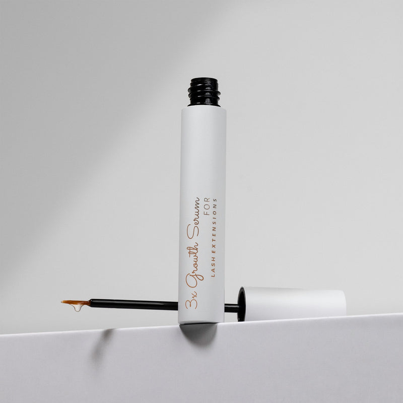 White bottle of lash growth serum with an open applicator resting on a white surface, against a neutral background.