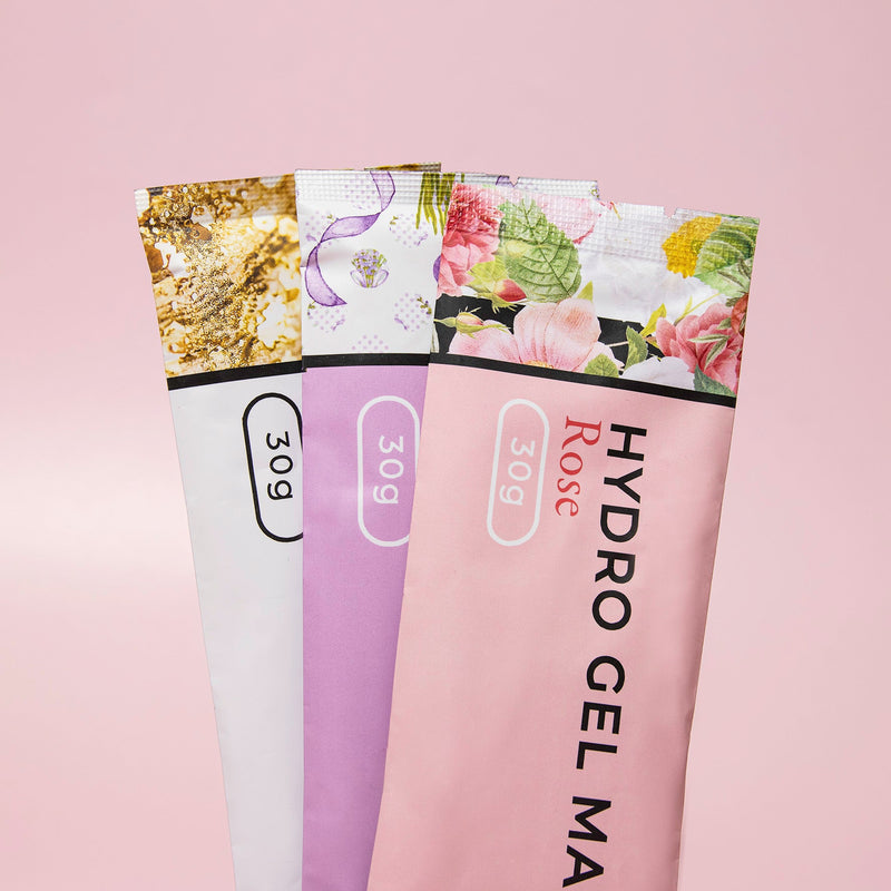 Three varieties of Hydro Gel Mask packages, stacked vertically: Gold Foil, Lavender, and Rose, each weighing 30g, displayed against a light pink background."