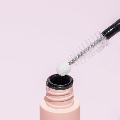 "Curacoro lash adhesive with a precision applicator, showcasing a pink background. The image highlights the white tip of the applicator, emphasizing the product's design for precise lash application.