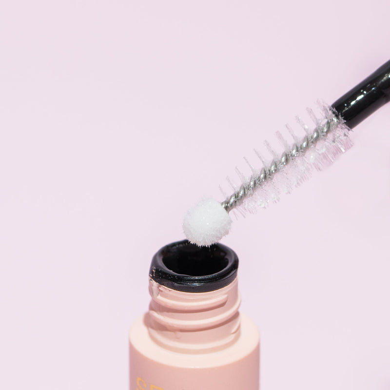 "Curacoro lash adhesive with a precision applicator, showcasing a pink background. The image highlights the white tip of the applicator, emphasizing the product&