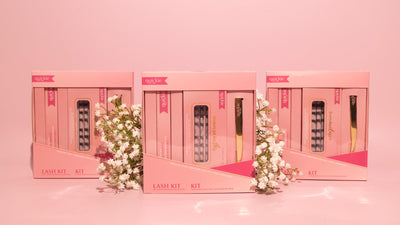 Three pink lash kit boxes arranged in a row, featuring DIY lash extension sets from Quickie by LLBA, with delicate white flowers in the foreground against a soft pink background.