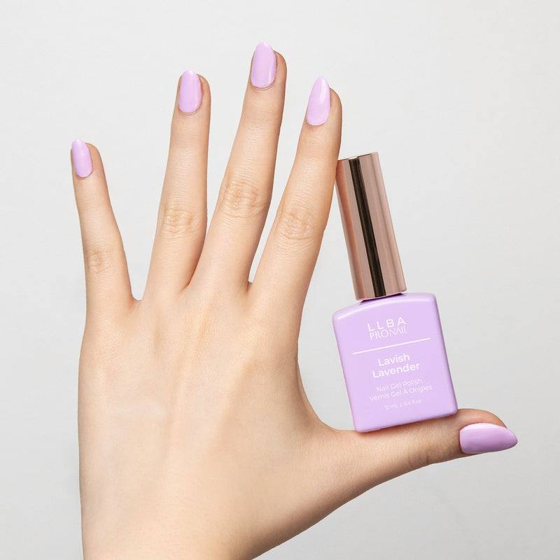 Hand holding a bottle of LLBA Pronail Lavish Lavender Nail Gel Polish, featuring a soft lavender shade, with matching nail color on the hand, against a light background.