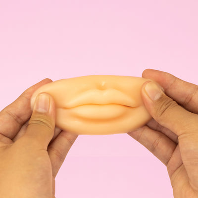 Hands holding a white 3D Silicone Lips. against a pink background.