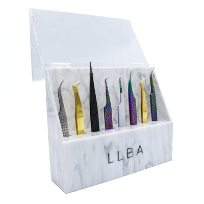 LLBA marble-designed tweezer holder with a clear lid, displaying various lash tweezers in gold, black, and iridescent finishes.