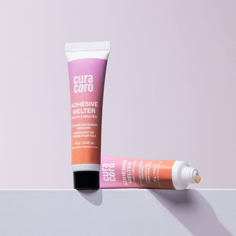 Two Curacoro adhesive melter tubes, one standing and one lying open, with adhesive visible, on a light background.