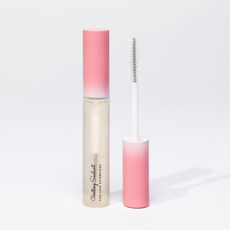 An open lash sealant tube with a clear applicator wand and a pink ombre cap, placed on a white surface with soft shadows.