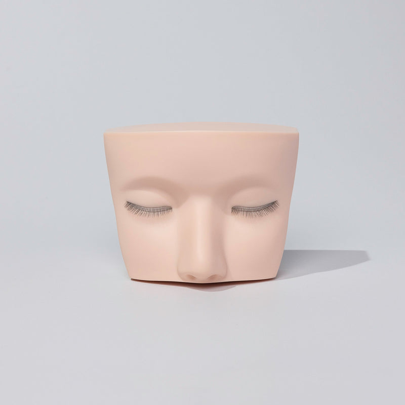 Mannequin head with multi-layered eyelash extensions on a neutral background, ideal for lash training and practice.