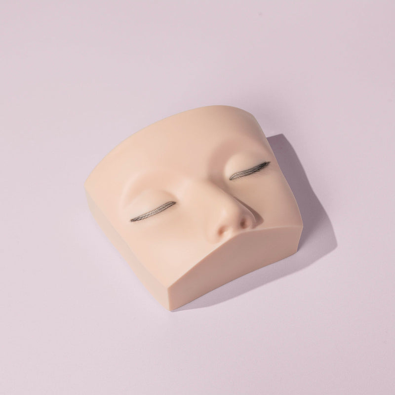 Mannequin head with multi-layered eyelash extensions on a light pink background, ideal for lash training and practice.