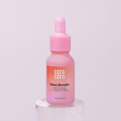 Curacoro Nano Bonder, 15 ml bottle, for maximizing eyelash extension retention, on a pink background.