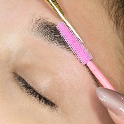 Image of using a disposable pink silicon brush to shape eyebrows.