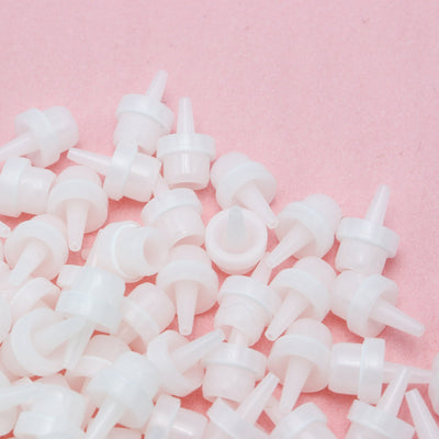 Adhesive nozzles for eyelash extension adhesive in front of a pink background.