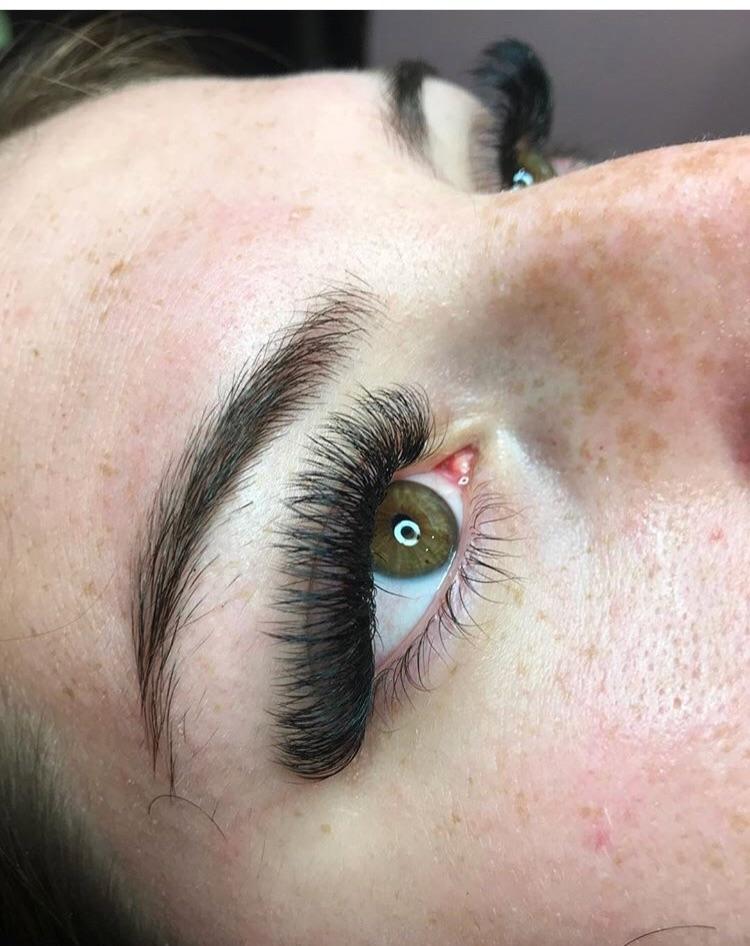 Close-up of a green eye with full, voluminous eyelash extensions, showcasing professional lash application.