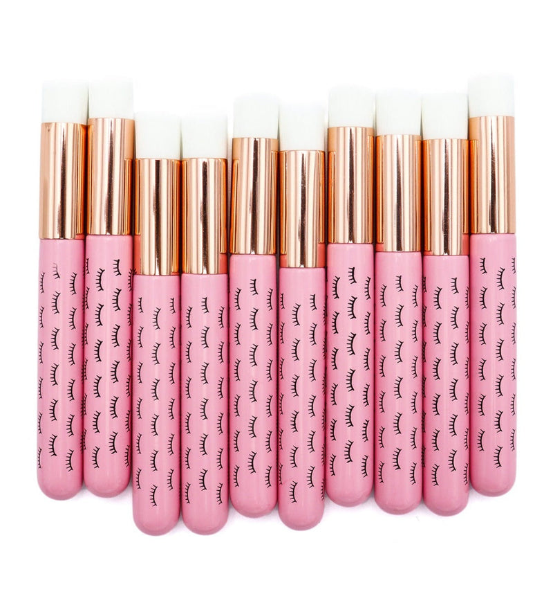 Ten pink wooden cleansing brushes over a white background